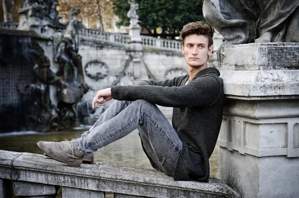 Handsome young man outdoors, sitting on old stone balusters — Stock Photo, Image