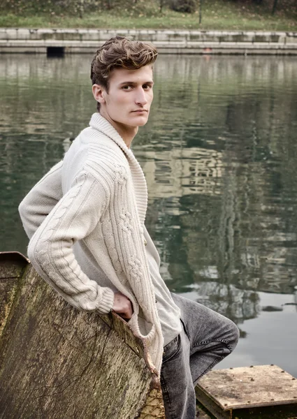 Attractive young man standing against rusty metal next to river — Stock Photo, Image