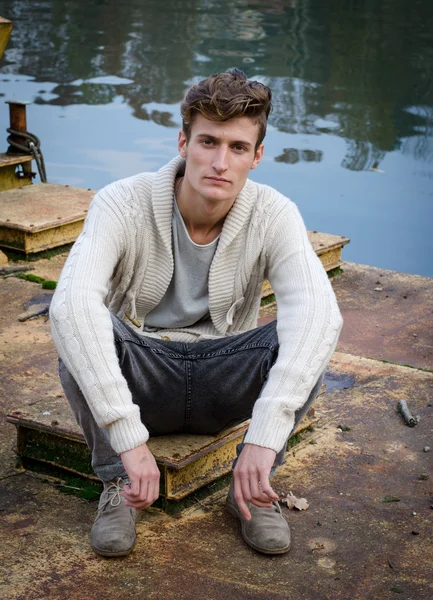 Attractive young man sitting on rusty metal next to river — Stock Photo, Image