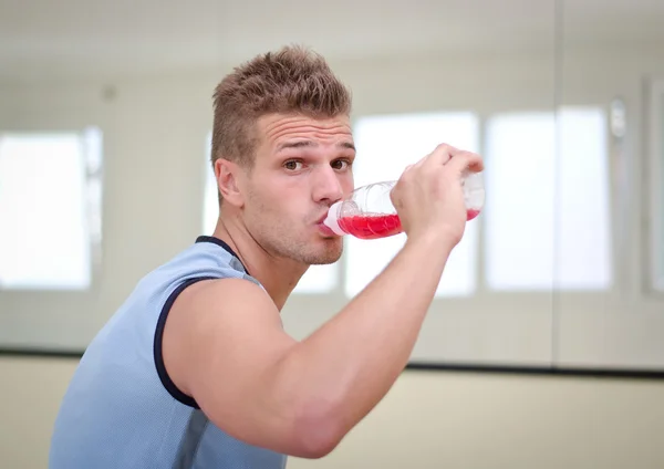 Vonzó, jó sportoló iszik piros ital palack — Stock Fotó