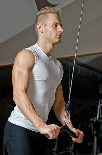 Handsome blond young man exercising triceps on gym equipment — Stock Photo, Image