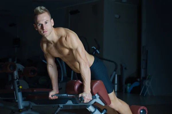 Shirtless young man exercising femural biceps on gym equipment — Stock Photo, Image