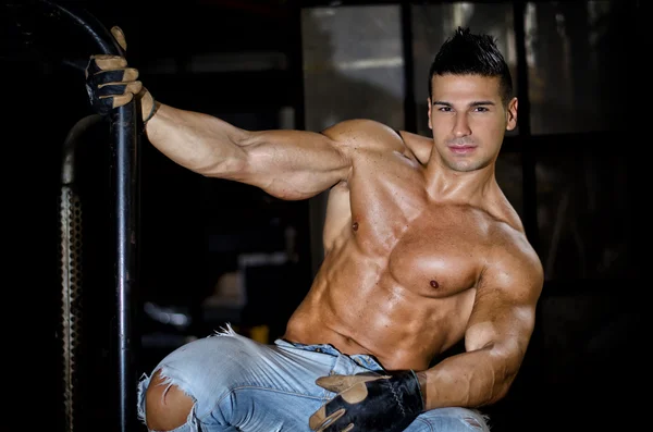 Muscular latino bodybuilder in jeans hanging from metal handle — Stock Photo, Image