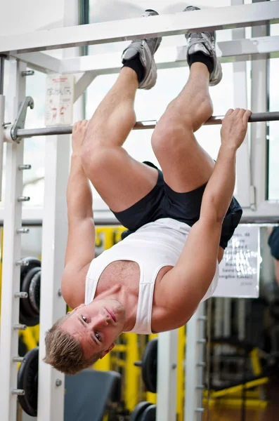 Young man in gym hanging upside-down to exercise abs — Stock Photo, Image