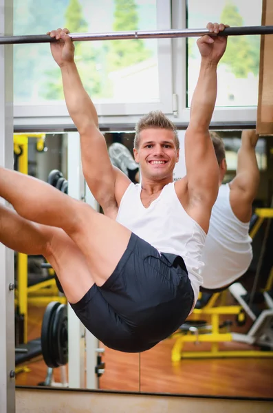 Smiling young man hanging from gym equipment — Stock Photo, Image