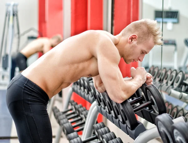 Young man resting on dumbbells rack after workout in gym — Stock Photo, Image