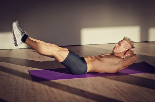 Bonito jovem fazendo exercícios abdominais no tapete — Fotografia de Stock