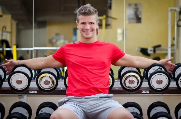 Vacker leende ung i gymmet sitter på hantlar rack — Stockfoto