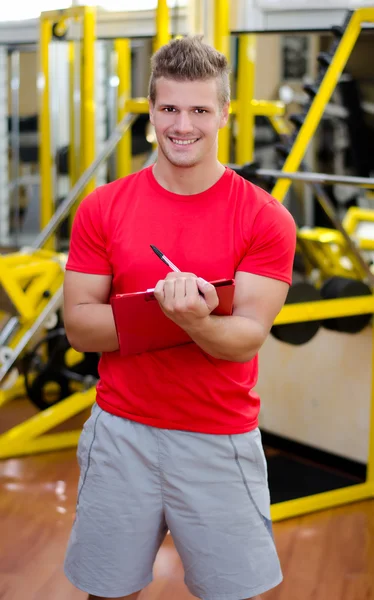Entrenador personal masculino joven escribiendo sobre portapapeles sonriendo —  Fotos de Stock