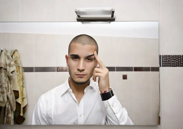 Knappe jonge man kijken naar zichzelf in badkamerspiegel — Stockfoto