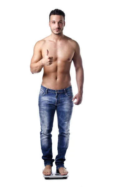 Muscular young man weighing himself on scale, making OK sign — Stock Photo, Image