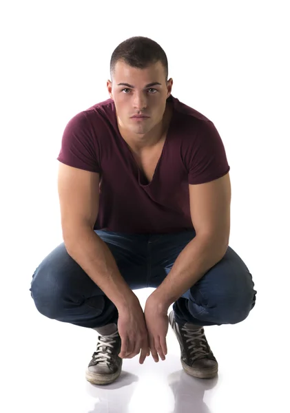 Joven guapo con camiseta y pantalones vaqueros sentado sobre sus talones —  Fotos de Stock