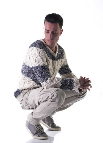 Goed uitziende jongeman met winter trui, zittend op zijn hielen — Stockfoto
