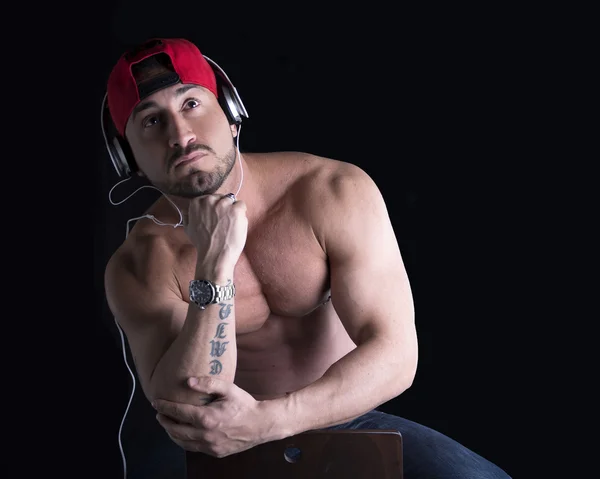 Hombre musculoso sentado, escuchando música con auriculares — Foto de Stock