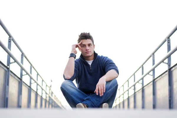 Handsome young man sitting between handrails in walkway — Stock Photo, Image