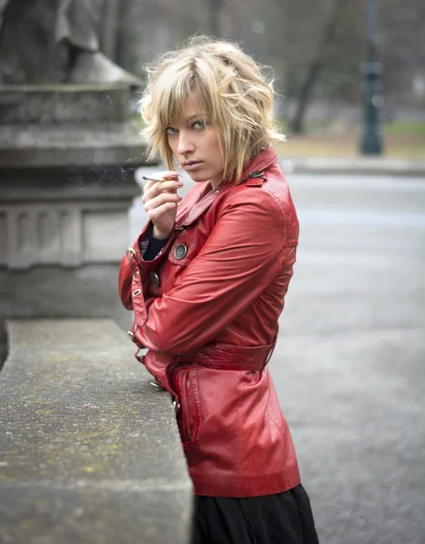 Mujer joven y bonita fumando, con chaqueta de cuero rojo — Foto de Stock