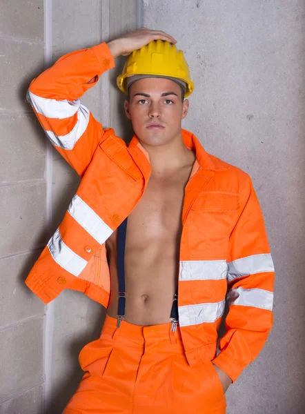 Красивый молодой строитель в оранжевом костюме, открытый на голом туловище — стоковое фото