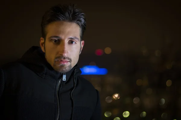 Aantrekkelijke jonge man portret met stadslichten achter hem 's nachts — Stockfoto