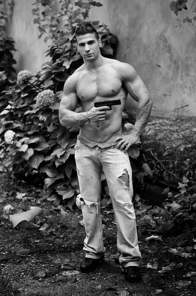 Muscular shirtless young man with a gun in his hand — Stock Photo, Image