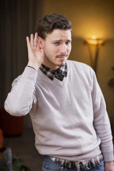 Knappe jonge man kan niet horen, zetten hand rond zijn oor — Stockfoto