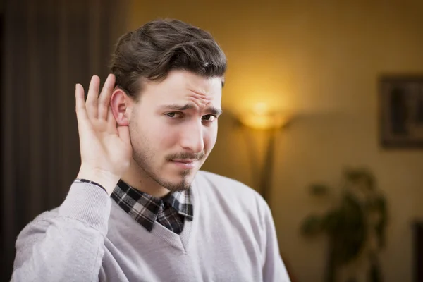 Knappe jonge man kan niet horen, zetten hand rond zijn oor — Stockfoto