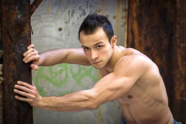 Muscular young man standing, leaning against rusty metal structure — Stock Photo, Image
