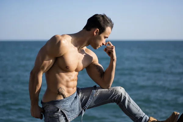Muscular shirtless young man standing by the sea or ocean — Stock Photo, Image