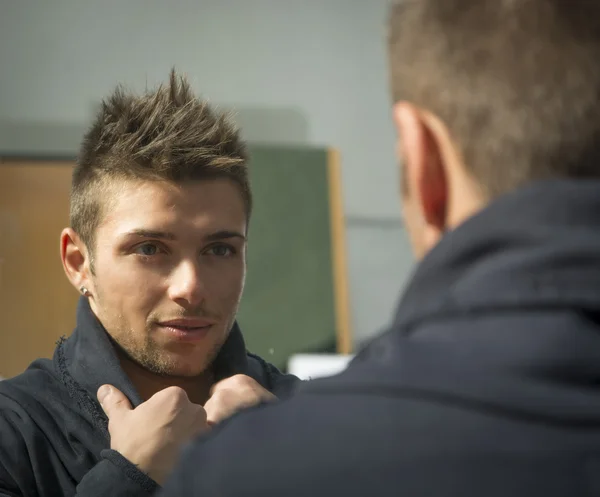 Handsome young man looking at himself in mirror — Stock Photo, Image