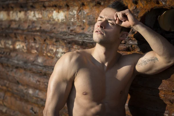 Muscoloso torso nudo giovane prendendo il sole sulla roccia da muro di metallo arrugginito — Foto Stock