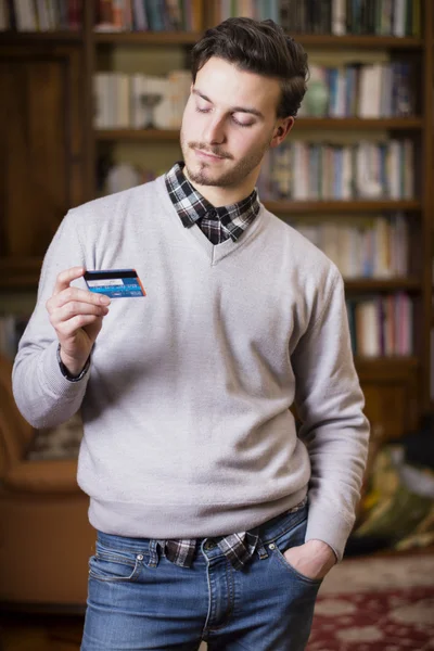 Attractive young man holding credit card, looking at it — Stock Photo, Image