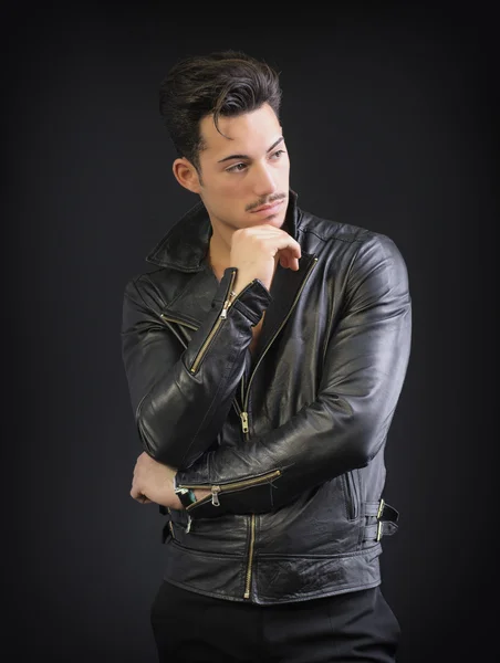 Attractive young man with leather jacket, on dark background, looking away — Stock Photo, Image