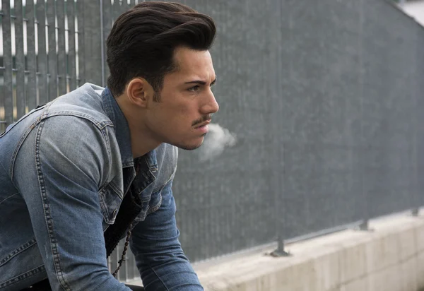 Trendy young man sitting outside smoking — Stock Photo, Image