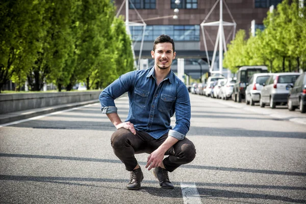 Attraente uomo sorridente seduto nel mezzo di strada della città — Foto Stock