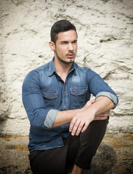 Handsome young man sitting outdoors in front of stone — Stock Photo, Image