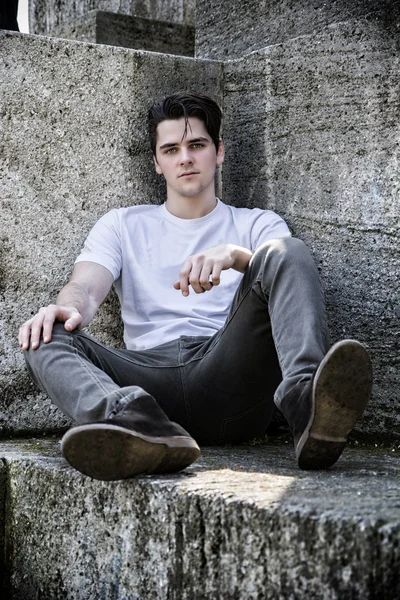 Atraktivní mladý muž sedí na kámen nebo mramor bloky — Stock fotografie