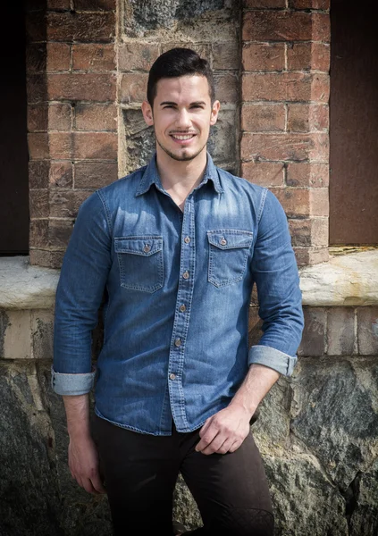 Όμορφος νεαρός άνδρας με το τζιν πουκάμισο στέκεται έξω, χαμογελώντας — Φωτογραφία Αρχείου