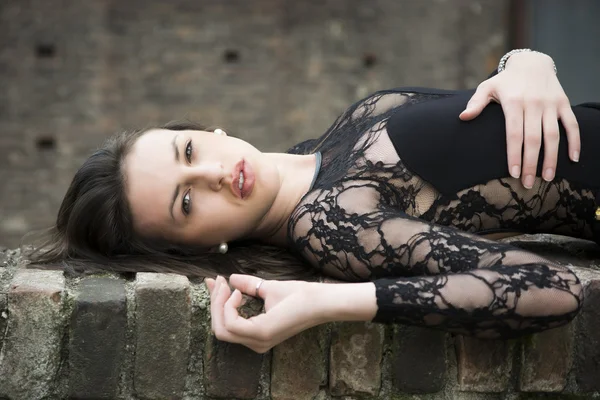 Pretty brunette young woman lying down on brick wall — Stock Photo, Image