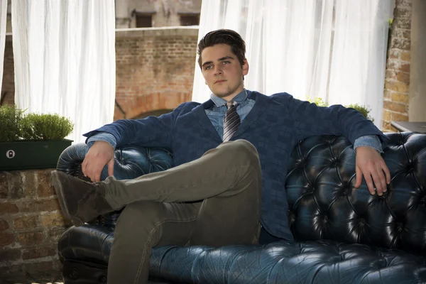 Atrakcyjny młody człowiek siedzi na kanapie elegancki — Zdjęcie stockowe