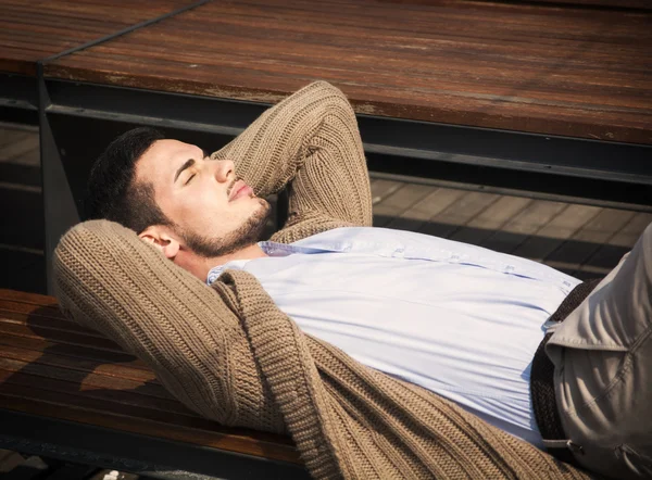 Atraktivní mladý muž, kterým se stanoví na dřevěné lavici — Stock fotografie