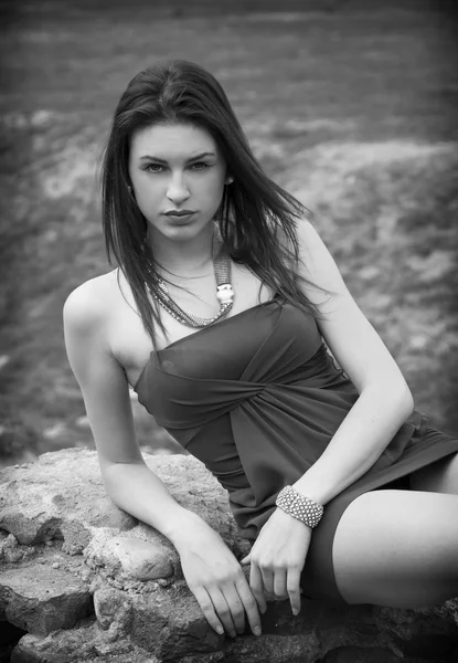 Aantrekkelijke jonge vrouw in grasland leunend op steen — Stockfoto