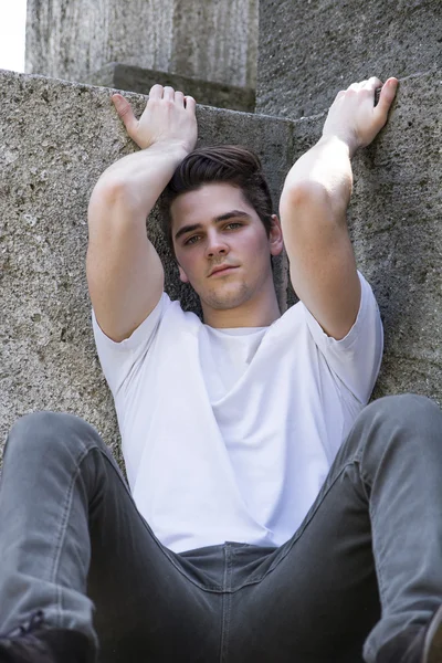 Atraktivní mladý muž sedí na zemi proti kamenných bloků — Stock fotografie
