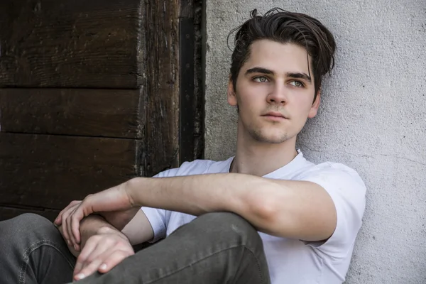 Attractive young man sitting on old door's threshold — Stock Photo, Image