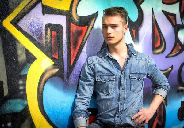 Handsome blond young man against colorful graffiti wall — Stock Photo, Image