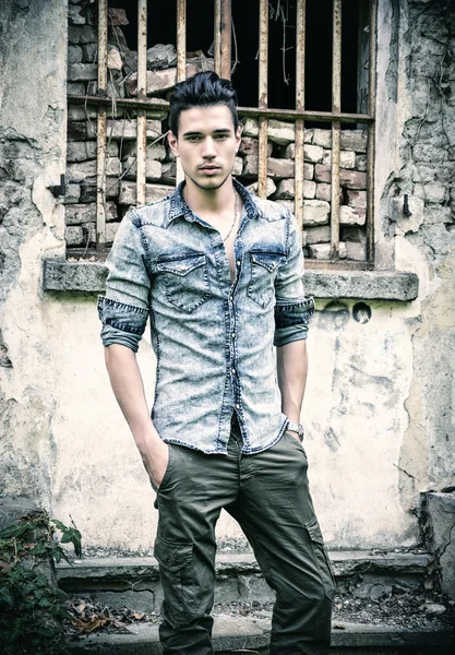 Attractive young man standing outdoor in front of abandoned house — Stock Photo, Image