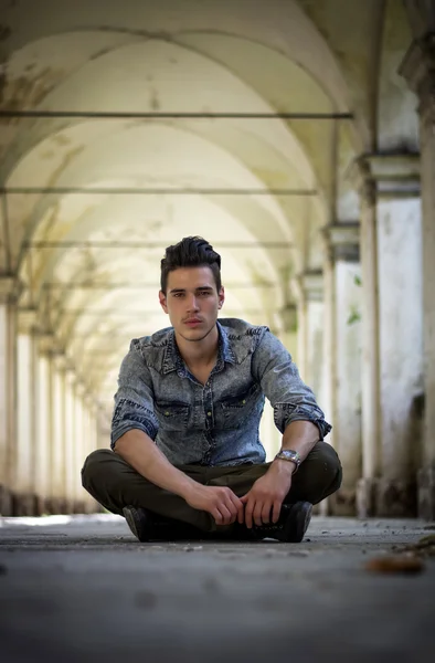 Handsome young man sitting under old colonnade — Stock Photo, Image