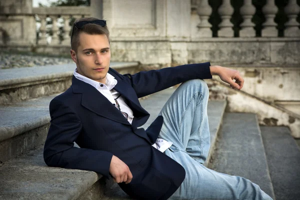 金发碧眼的年轻英俊男子，坐在外面的石楼梯台阶上 — 图库照片