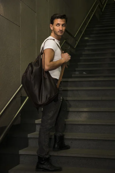 Joven guapo de pie con una bolsa grande en la escalera — Foto de Stock