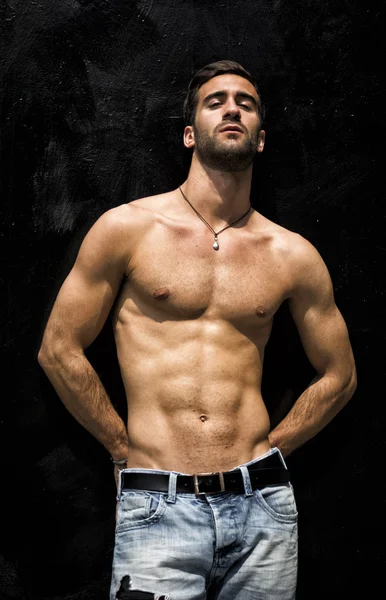 Handsome bearded shirtless young man standing against black wall — Stock Photo, Image