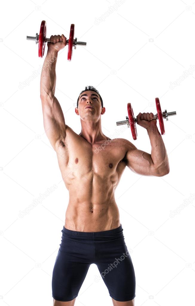 Muscular shirtless young man exercising shoulders with dumbbells