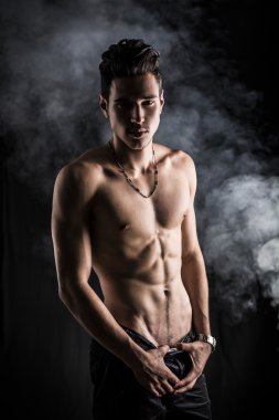 Yalın atletik gömleksiz genç adam koyu arka plan üzerinde duran